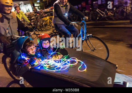 Cambridge, UK. 9th Feb, 2018. Cyclists with decorated bicycles parade around the market square as part of the e-Luminate Cambridge Festival 2018. e-Luminate Cambridge is a contemporary arts festival for a city at the forefront of scientific and technological research. The event shows the diversity of Cambridge’s iconic buildings and public spaces in a new light. Light crosses both Art and Science, and the Festival is a celebration of the infinite possibilities created by this intersection. Credit: Julian Eales/Alamy Live News Stock Photo