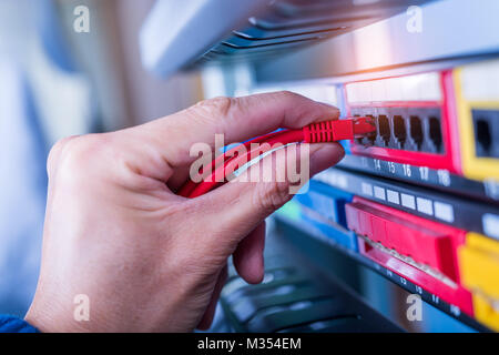administrator holding network cables connected to servers Stock Photo