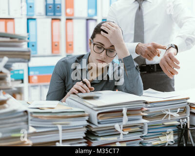 Demanding boss pointing to his watch and asking to his employee to hurry up, his secretary is frustrated and overwhelmed by work: business and deadlin Stock Photo