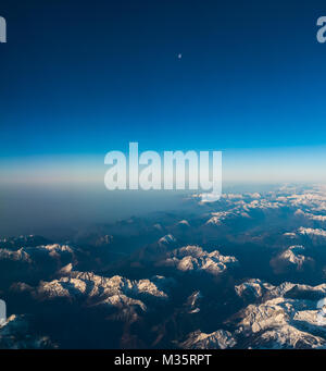 Looking through the window aircraft during flight a snow covered Italian and Osterreich Alps with blue sky without clouds. Stock Photo