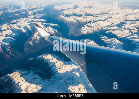Looking through the window aircraft during flight a snow covered Italian and Osterreich Alps with blue sky without clouds. Stock Photo