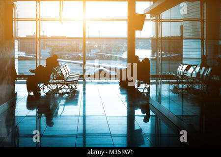 Silhouette of a unrecognizable travelers with backpack in international airport waiting lounge hall. Stock Photo
