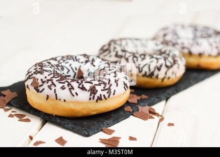 Three white donuts with chocolate sprinkles on black slate stone serving tray Stock Photo
