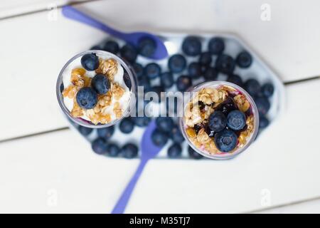 Top down view on two blueberry yogurt parfaits in tall glasses on white wooden table Stock Photo