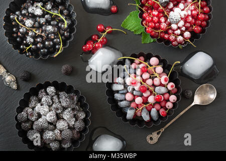Frozen red currant garnish of ice, branch red currant in dark plate on a black background. Stock Photo