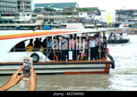Hand of photographer with smart phone shooting image on blurred passenger on boat background. Stock Photo