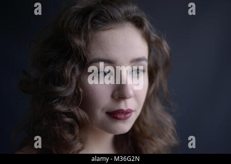 Dark haired vintage styled girl in a red coat with red lips- isolated on a very dark grey background Stock Photo