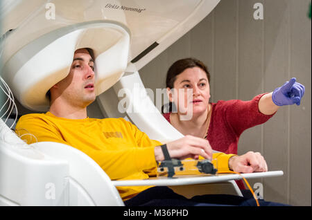 Physicist Anda Popescu directs a subject to perform various tasks as a scanner measures changes in magnetic fields generated by his brain in the Magnetoencephalography (MEG) Laboratory at the National Intrepid Center of Excellence (NICoE) at Walter Reed National Military Medical Center in Bethesda, Md., Mar. 21, 2017. Unlike its cousin, the more commonly used electroencephalography (EEG), the MEG brain scan can see changes in structures that reside deep in the brain tissue. By measuring minute changes in magnetic fields generated by the cerebral cortex while resting, while thinking and while e Stock Photo