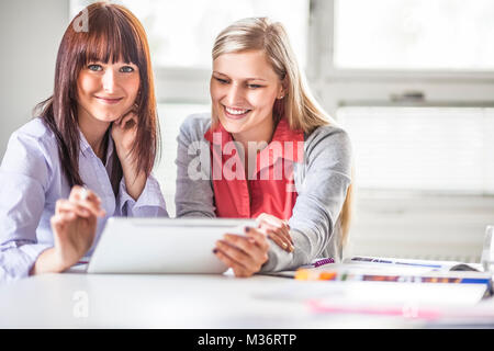 Portrait of young businesswoman with female colleague using digital tablet in office Stock Photo