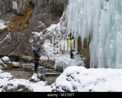 male ice climber in a yellow jacket on a steep frozen waterfall ice climbing in Sottoguda in the Dolomites Stock Photo