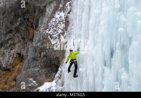 male ice climber in a yellow jacket on a steep frozen waterfall ice climbing in Sottoguda in the Dolomites Stock Photo