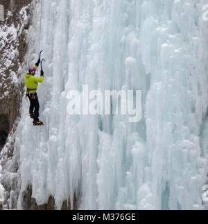 male ice climber in a yellow jacket on a steep frozen waterfall ice climbing in Sottoguda in the Dolomites Stock Photo