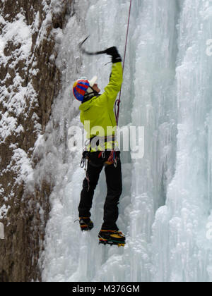 male ice climber in a yellow jacket on a steep frozen waterfall ice climbing in Sottoguda in the Dolomites Stock Photo