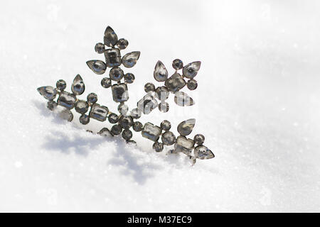 Glittery snowflake ornament in fresh powdery snow on a sunny day. Stock Photo