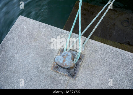 Ropes tying boat to iron dock bollard Stock Photo