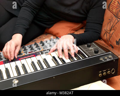 Woman lying on a sofa and playing synthesizers, indoor closeup Stock Photo