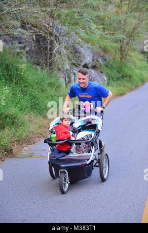 KENNESAW, Ga., Sept. 30, 2017 – Georgia Army National Guard Maj. John Harrison pushes his son during the final mile of the sixth annual Assault on Kennesaw Mountain 5K. The run takes place at the Kennesaw Mountain National Battlefield Park and commemorates the 42 Georgia Army National Guard Soldiers lost during the Global War on Terrorism from 2001 to present. Georgia National Guard photo by Capt. Charlie Emmons / released Riding to the Top by Georgia National Guard Stock Photo