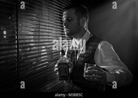 Gangster holding a bottle of whisky and glass while looking out the window Stock Photo