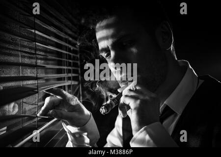 Gangster smoking a cigar while looking out the window at a car headlights Stock Photo