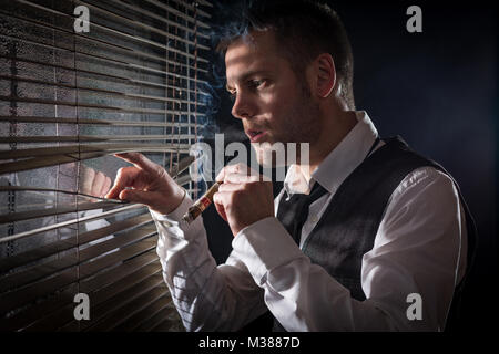 Gangster smoking a cigar while looking out the window at a car headlights Stock Photo