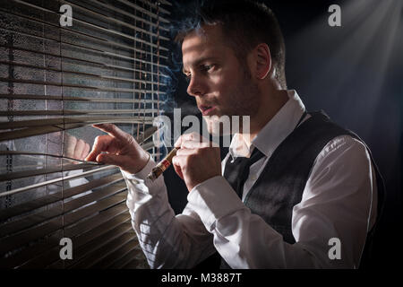 Gangster smoking a cigar while looking out the window at a car headlights Stock Photo