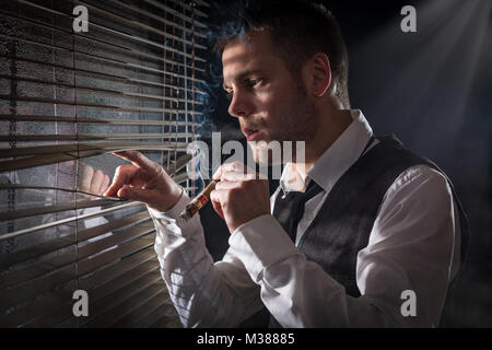 Gangster smoking a cigar while looking out the window at a car headlights Stock Photo