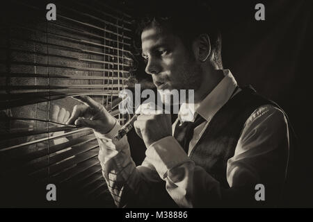 Gangster smoking a cigar while looking out the window at a car headlights Stock Photo