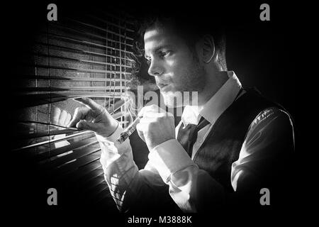 Gangster smoking a cigar while looking out the window at a car headlights Stock Photo