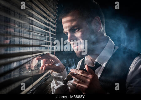 Gangster smoking a cigar while looking out the window at a car headlights Stock Photo