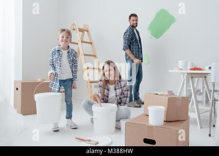 Family doing a home makeover, the man is painting the walls using a paint roller, the boy is carrying a paint bucket Stock Photo