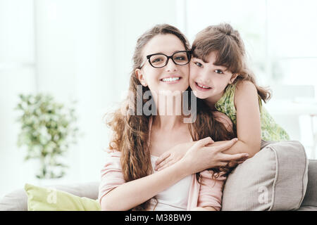 Happy family at home: a mother and her daughter are posing together in the living room and smiling, they are hugging Stock Photo