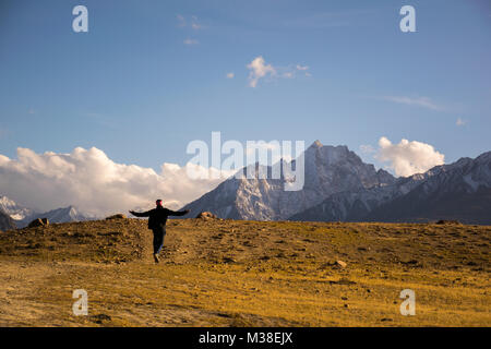 A man walking happily with his arms raised through a path surrounded by high mountains Stock Photo