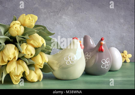 Easter composition with yellow tulips and ceramic hens with Easter eggs in green, yellow and gray colors Stock Photo