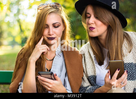 Female friends looking at smart phone on a park bench Stock Photo