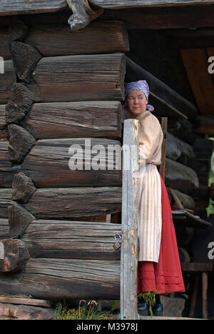 Young woman in old traditional dress at the entrance of a wooden house, Skansen Open-Air Museum, Stockholm, Sweden Stock Photo