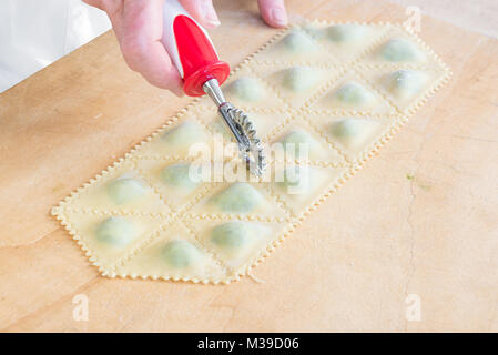 Traditional Italian pasta. Preparation phase of tortelli with spinach and ricotta using a dough cutter (cutter wheel) Stock Photo