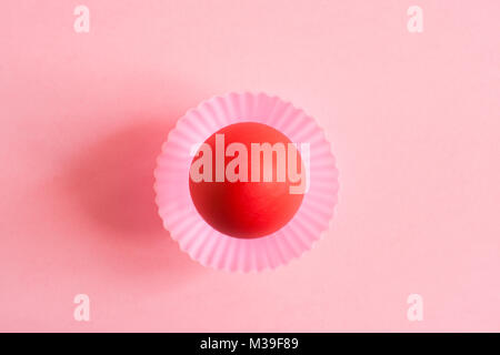 One Easter red painted egg in pink carved cupcakes mold in the middle of a pink background with copy space. Top view. Stock Photo
