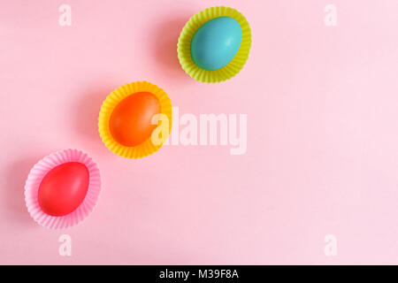 Easter background. Flat lay three colorful painted eggs in pink carved cupcakes molds are diadonally lying on a pink background with copy space.