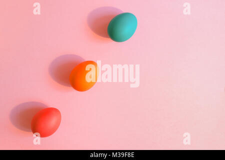 Flat lay three Easter  colorful painted eggs are lying diagonally on a pink background with copy space.