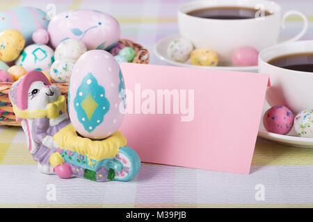 Easter figurine and egg and blank envelope with cups of coffee and Easter basket in background Stock Photo
