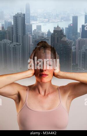 MODEL RELEASED. Conceptual composite image of woman covering ears with eyes closed against backdrop of city. Stock Photo
