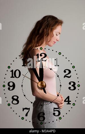 MODEL RELEASED. Composite image of woman holding her stomach with her biological clock ticking. Stock Photo