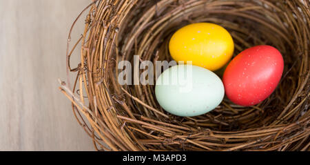 Close up of colorful Easter eggs in a rustic nest or basket on wooden background. Flat Lay, top view, high angle with copy space. Natural light. Stock Photo