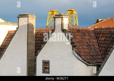 Leith, Edinburgh, Scotland, United Kingdom. Incongruous juxtaposition of huge yellow sunlit wind turbine platforms, called windfarm jackets, in Leith harbour towering over the pantile roof of one of the oldest buildings in Leith, 17th century Lamb's House, a former Hanseatic Leith Merchant house, now home to the architect who restored it, Nicholas Groves Raines. These platforms arrive in Leith on their way North to provide a sub structure for turbines in an offshore wind farm in the Moray Firth Stock Photo