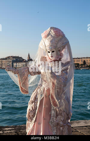 Venice, Veneto, Italy, 10th February 2018. Colourful costumes at the Venice Carnival on a sunny day on the last weekend of the festival. Woman posing on San Giorgio Maggiore Island at sunset. Stock Photo