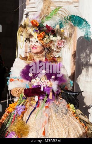 Venice, Veneto, Italy, 10th February 2018. Colourful costumes at the Venice Carnival on a sunny day on the last weekend of the festival. Woman in a classical costume with colourful accessories posing at the Doges Palace. Stock Photo