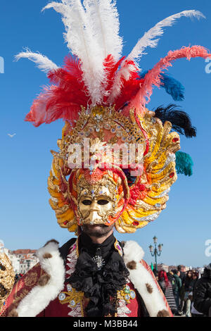 Venice, Veneto, Italy, 10th February 2018. Colourful costumes at the Venice Carnival on a sunny day on the last weekend of the festival. Man wearing an elaborate mask with feathers close up against a blue sky. Stock Photo