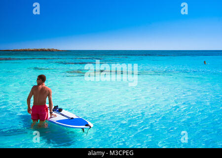 Tropical sandy beach with turquoise water, in Elafonisi, Crete, Greece. A young man with surf sup board Stock Photo