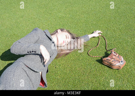 A beautiful girl wearing a tailored stylish patterned suit is at a Cricket Ground on a beautiful bright day- she is lying on the grass Stock Photo