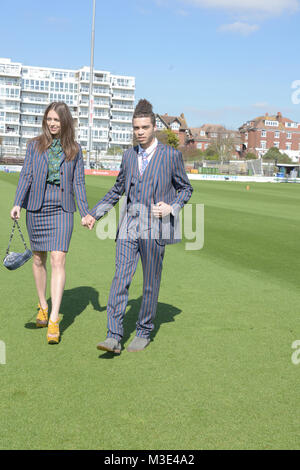 A beautiful girl wearing a tailored suit and a handsome mixed race guy in a suit walk aroungd a cricket ground on a bright day Stock Photo